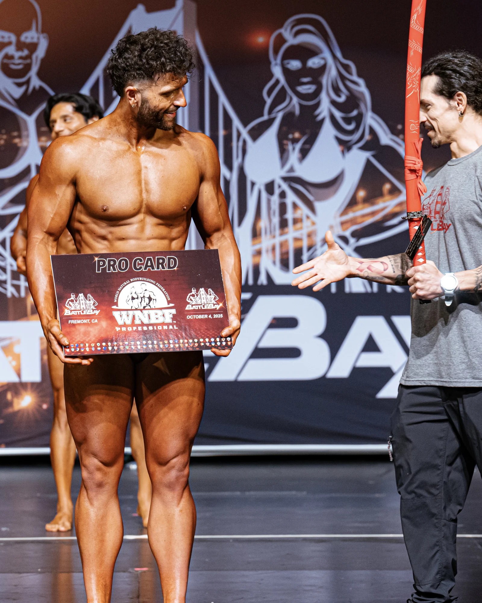 Ryan holding his WNBF professional pro card on the Battle of the Bay stage
